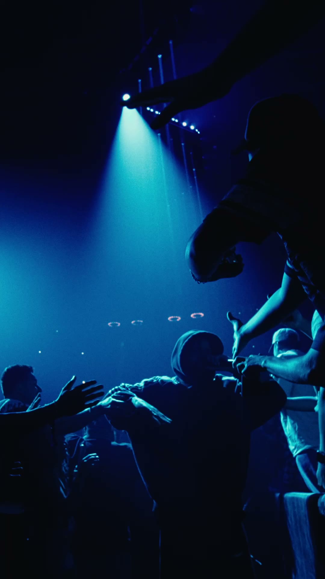 Blue-lit stage with reaching hands from the crowd